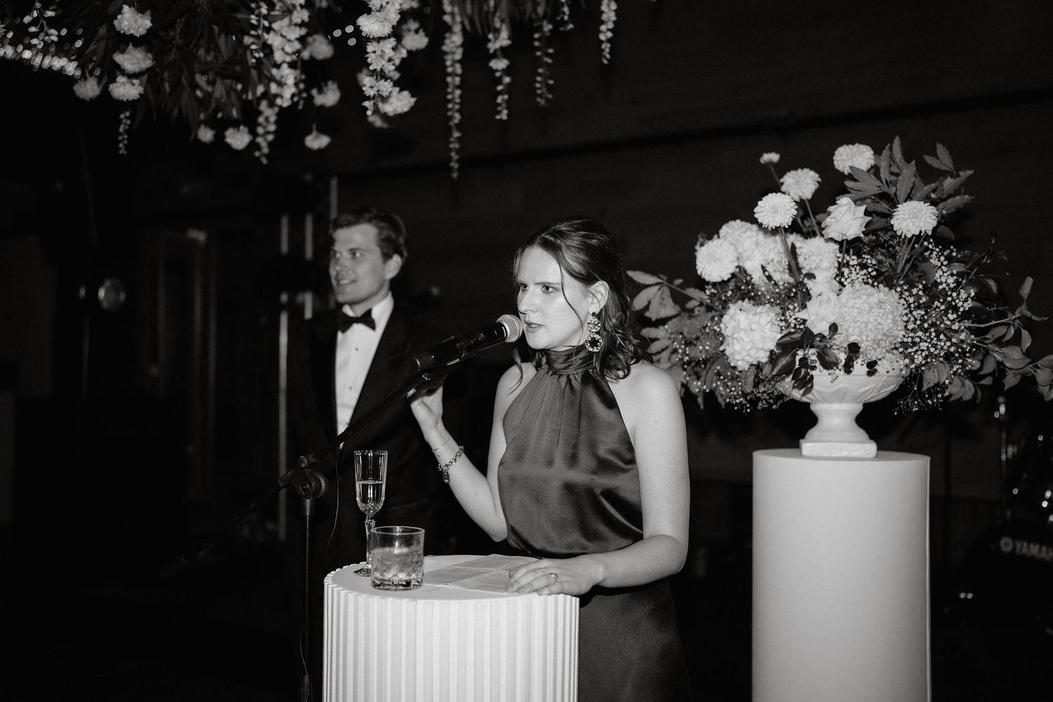 A black and white wedding reception photo showing a couple at a table with elegant floral centerpieces and decorations.