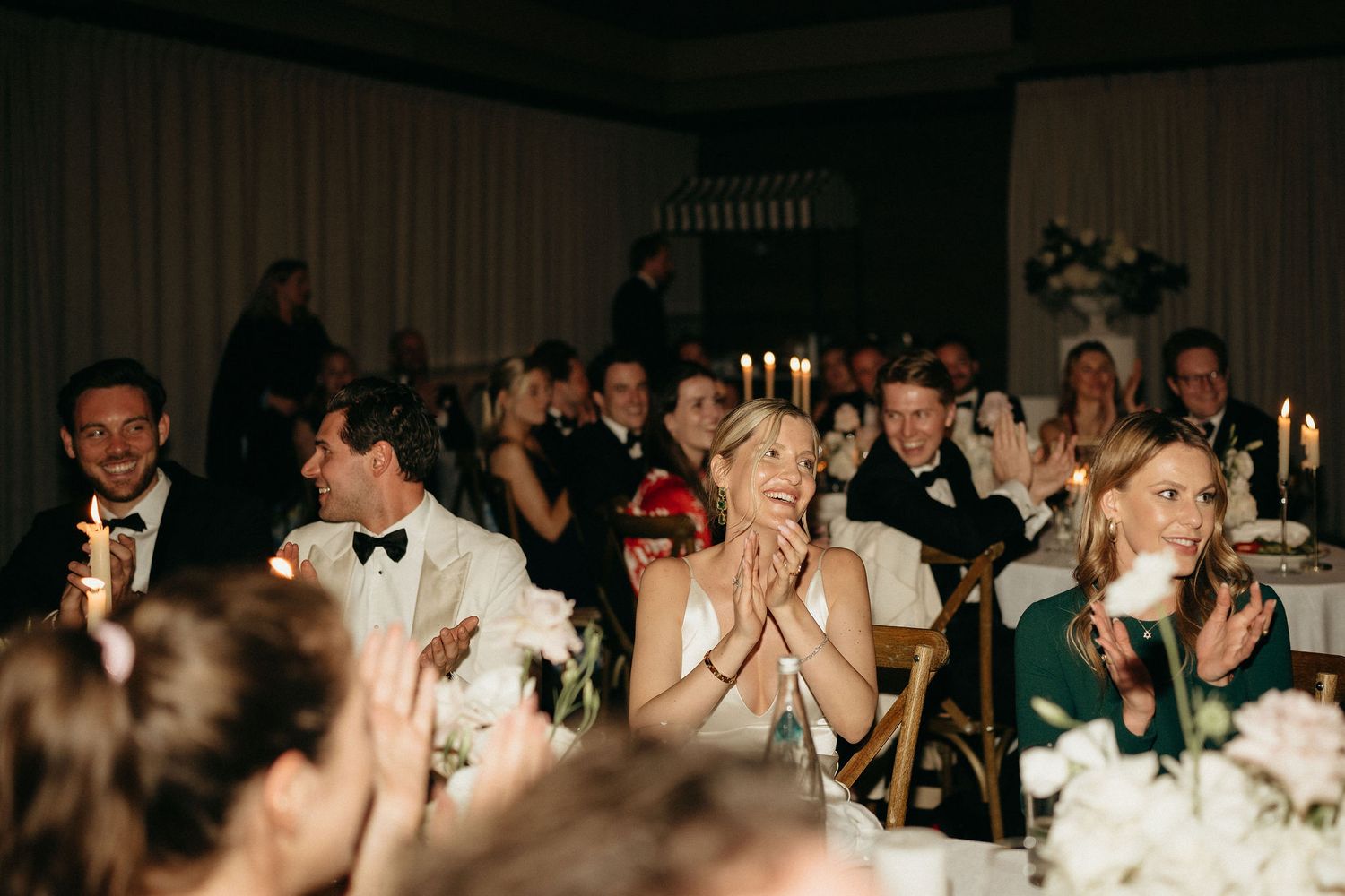Panoramic view of wedding celebration showing guests seated at long tables with candlelit decor in dark banquet hall.
