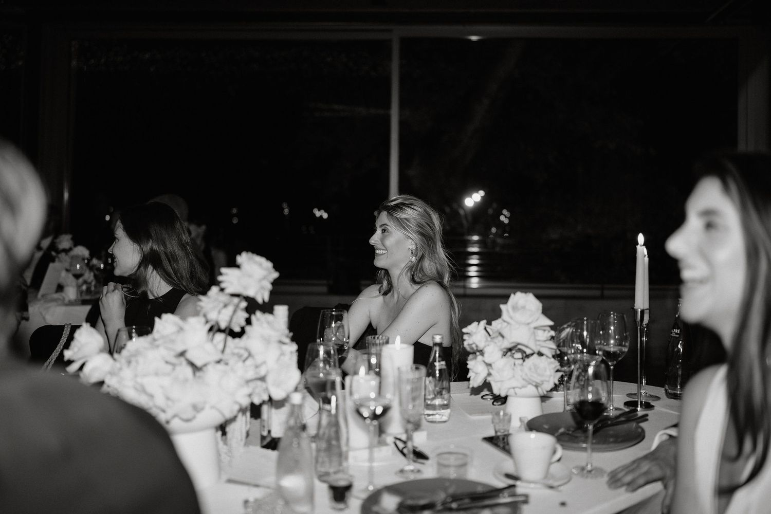 Wedding reception tables decorated with white floral centerpieces and glowing candlelight in dimly lit venue.