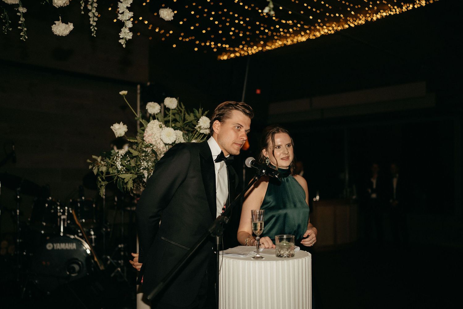 A couple shares a romantic moment on the dance floor at an evening wedding reception under twinkling lights.