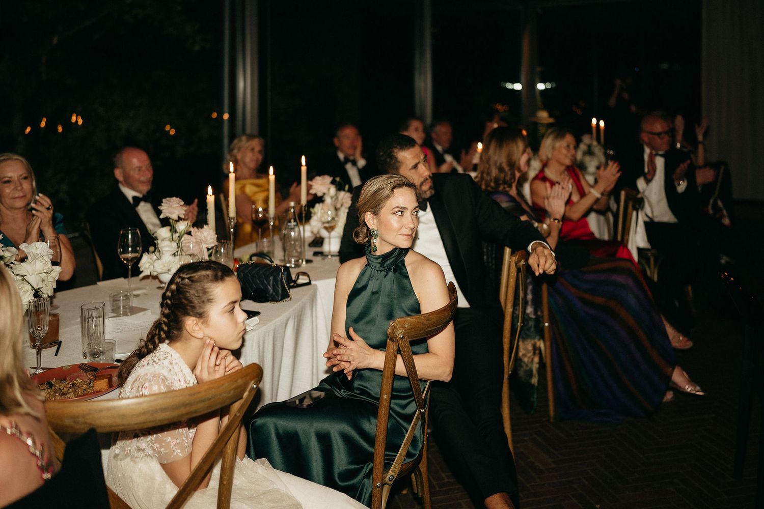 Wedding reception guests enjoy a candlelit dinner at elegantly decorated tables in a dimly lit venue.