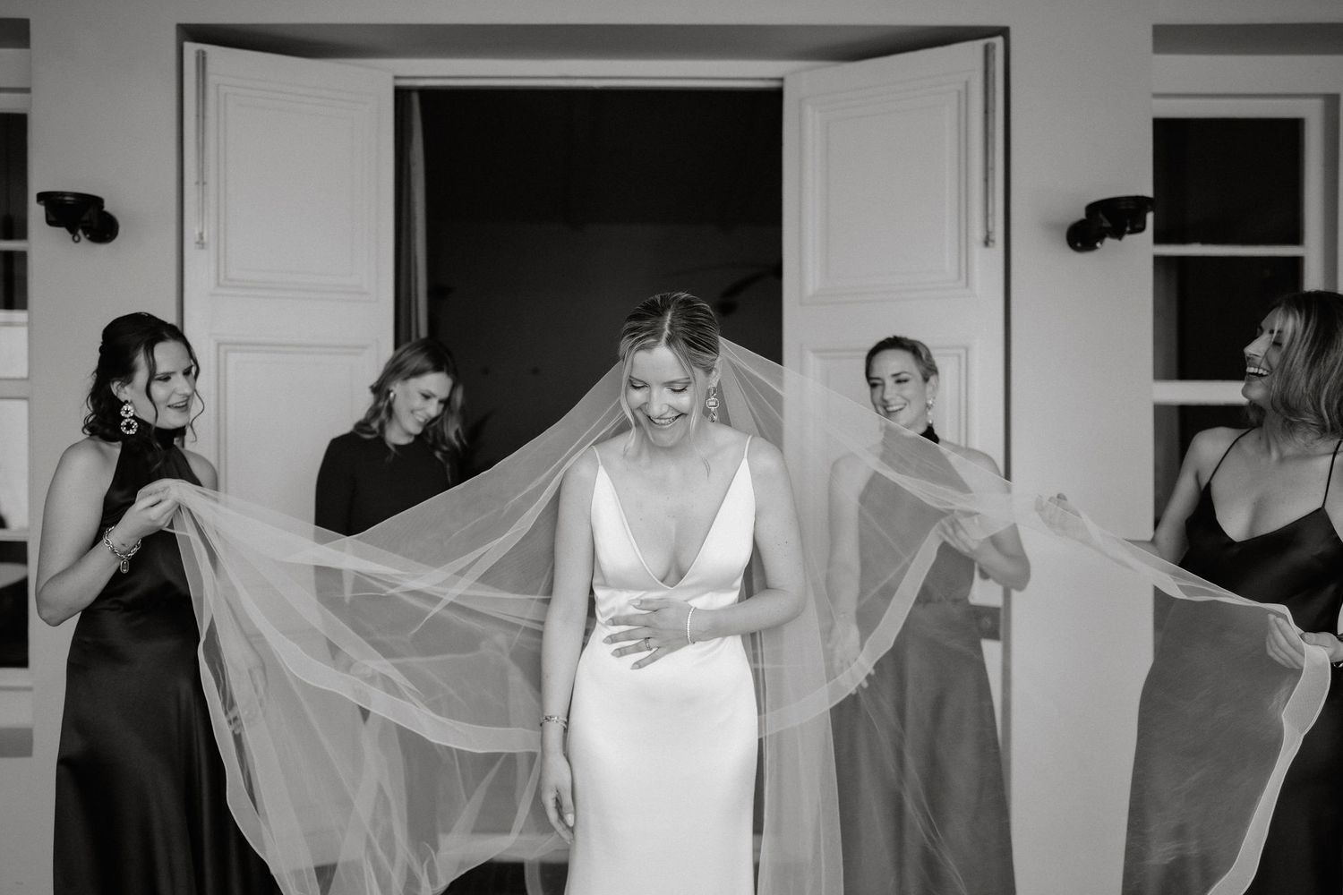 A black and white wedding photo series showing a bride getting ready with her veil flowing in multiple frames.