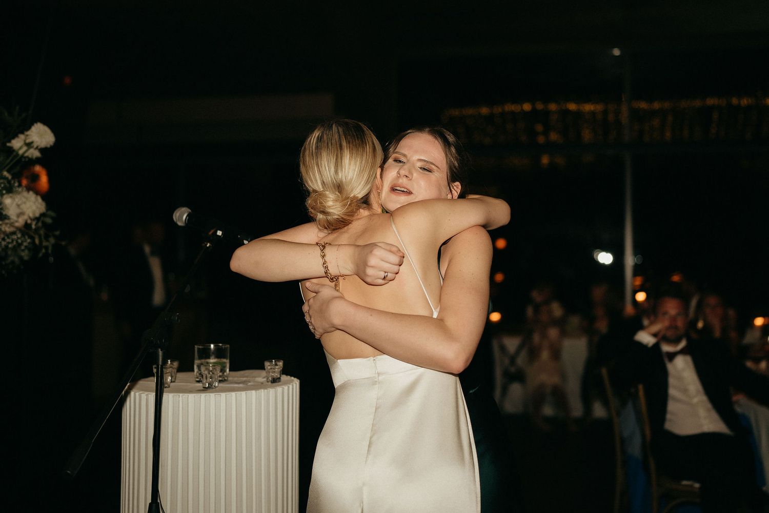 Two people share an emotional embrace during a dimly lit evening celebration.