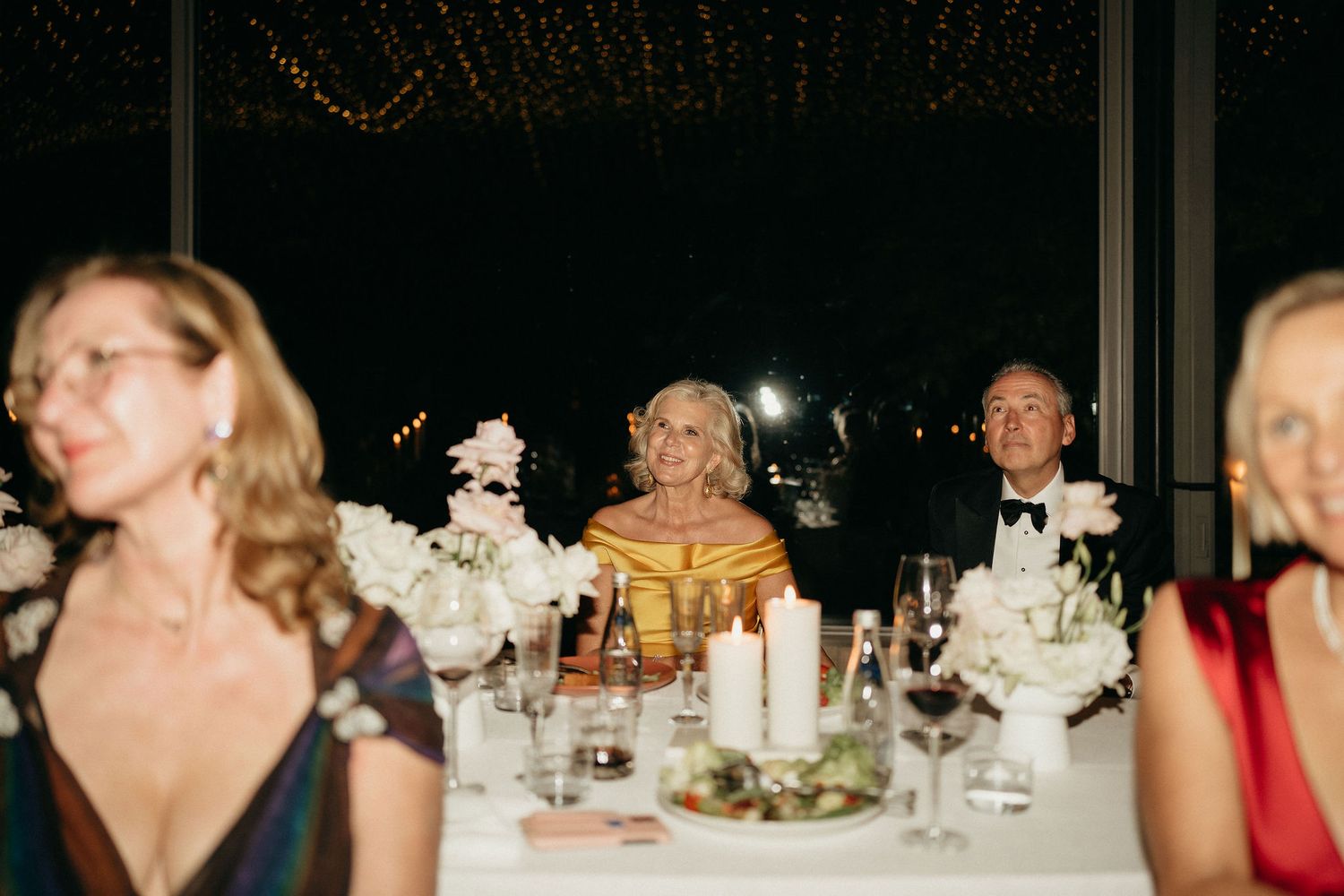 Guests seated at an elegant wedding reception dinner with white floral centerpieces and candlelit tables.