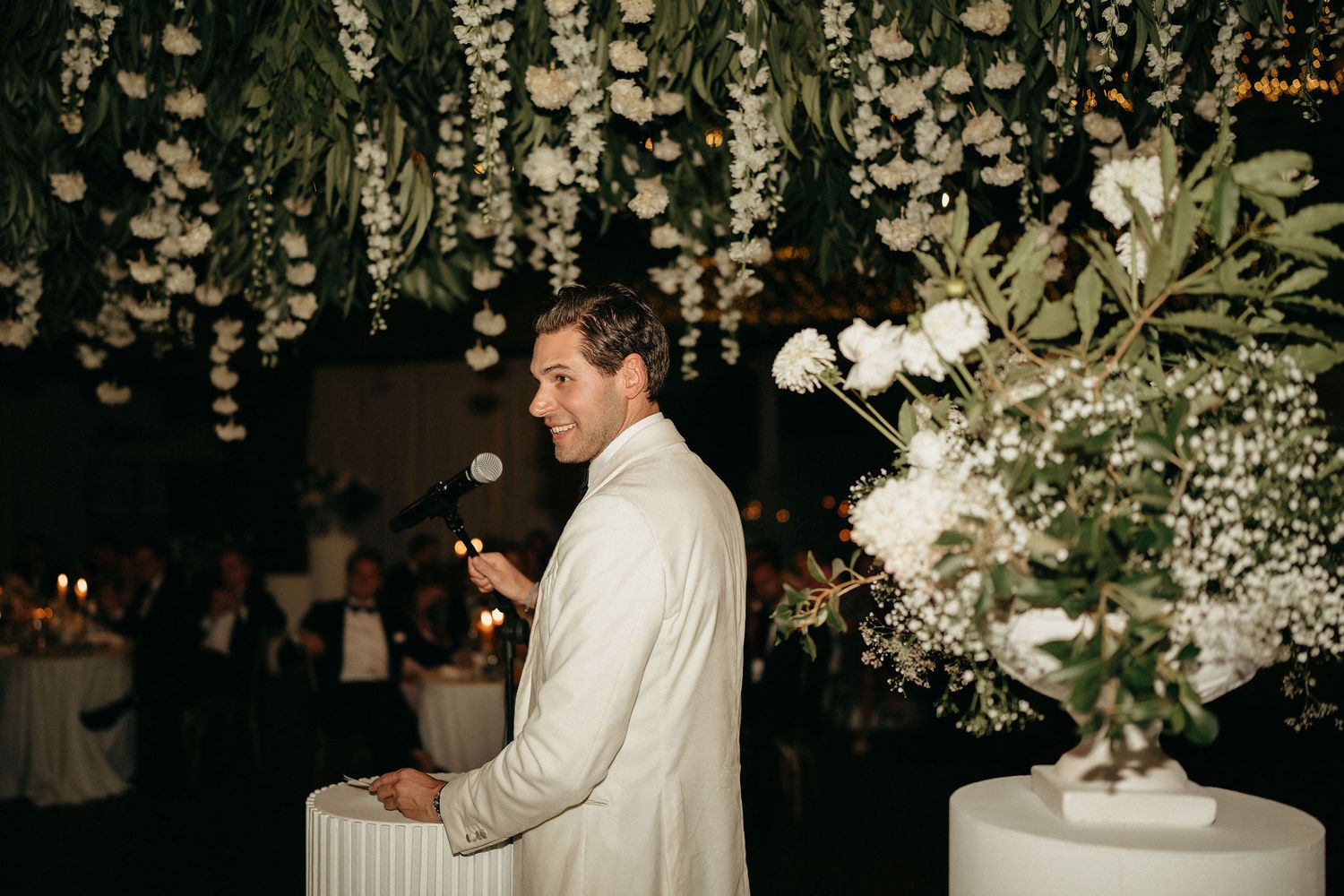 Romantic wedding reception setting with hanging floral decorations and white table arrangements.