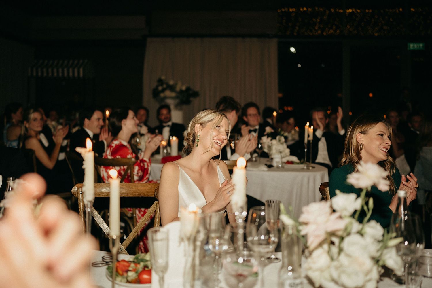 Wedding reception guests enjoy an elegant dinner celebration at round tables decorated with white linens and centerpieces.