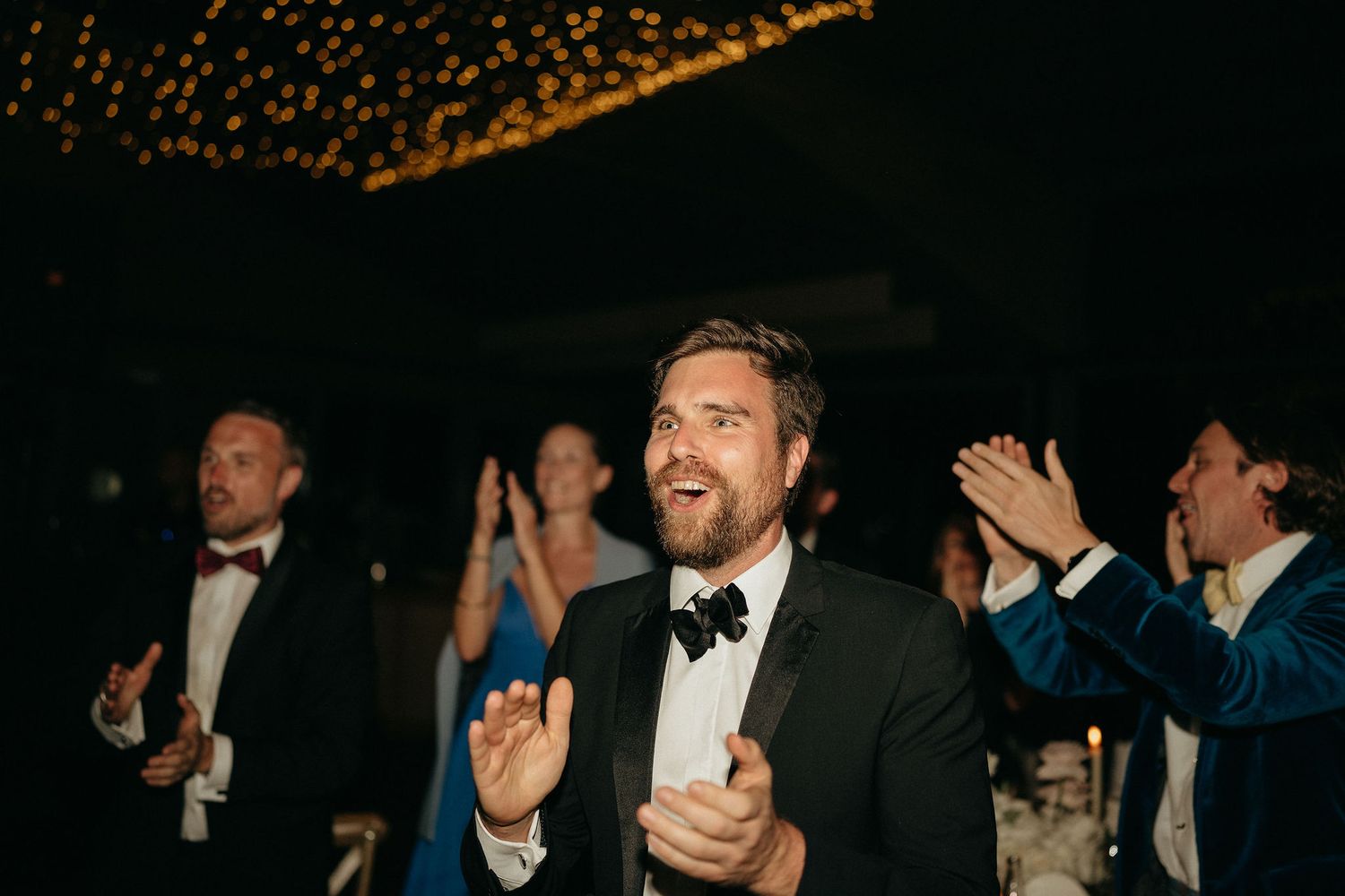 Formal event attendees in black tie attire applaud and celebrate during an elegant evening gathering.