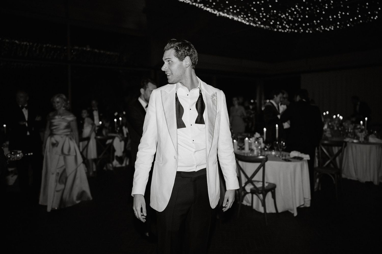 Black and white photo of couples dancing together at an elegant evening event with twinkling lights in the background.