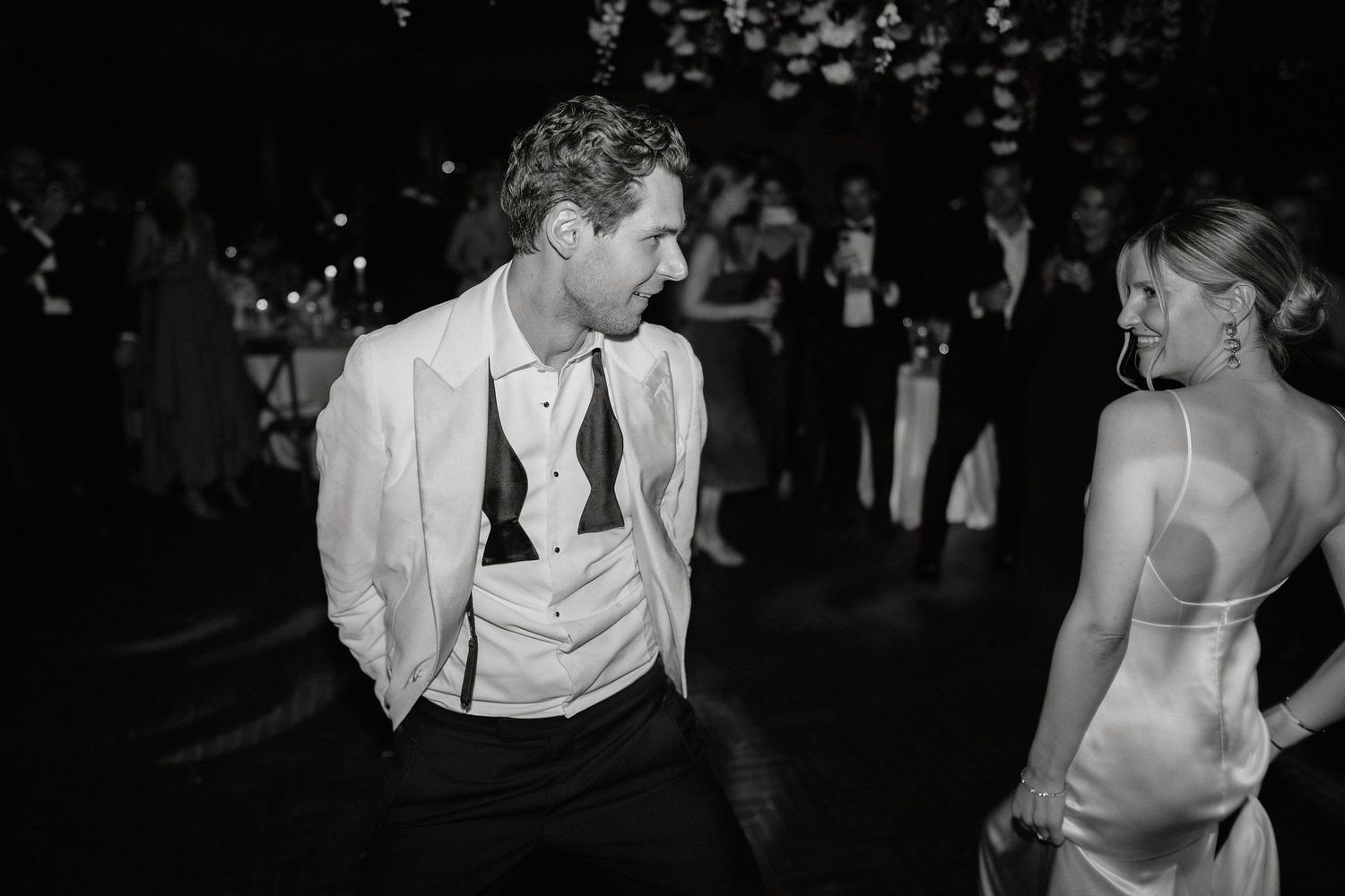 Couples dancing in formal attire at a dimly lit reception with romantic string lights overhead.