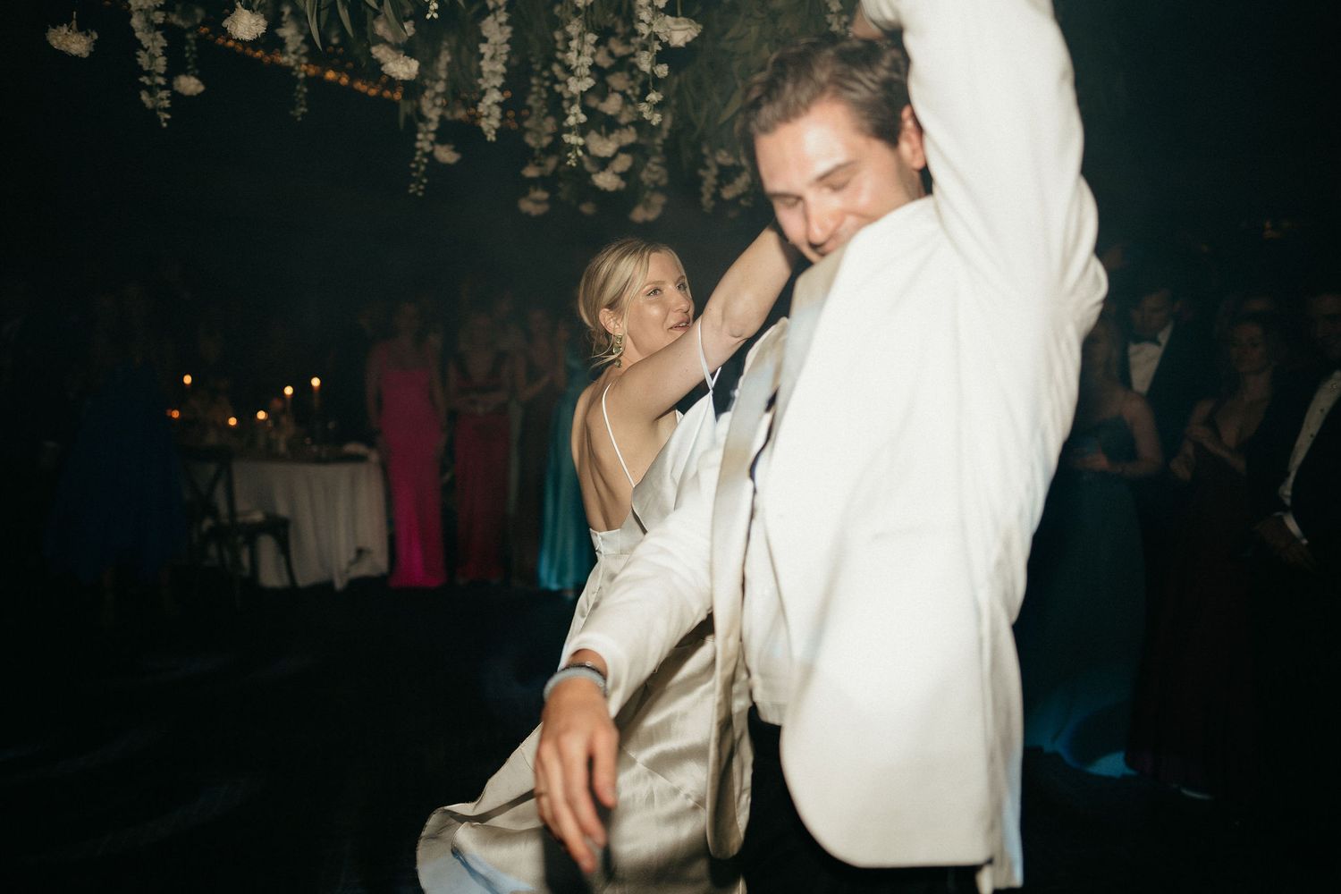 Couple dancing together at a wedding reception with the groom wearing a white suit jacket.