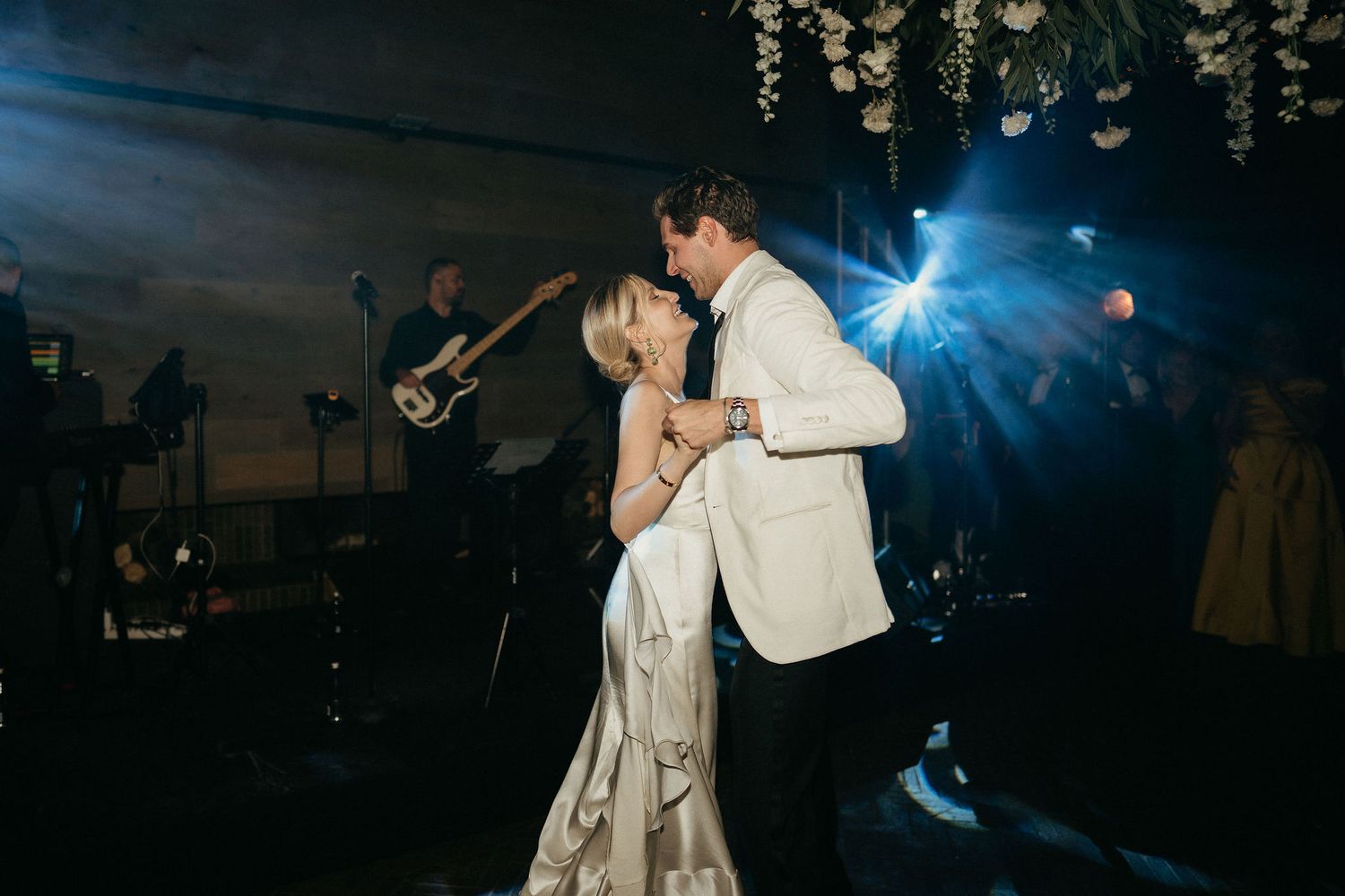 Newlyweds dancing together at their wedding reception under moody blue lighting and hanging decor.