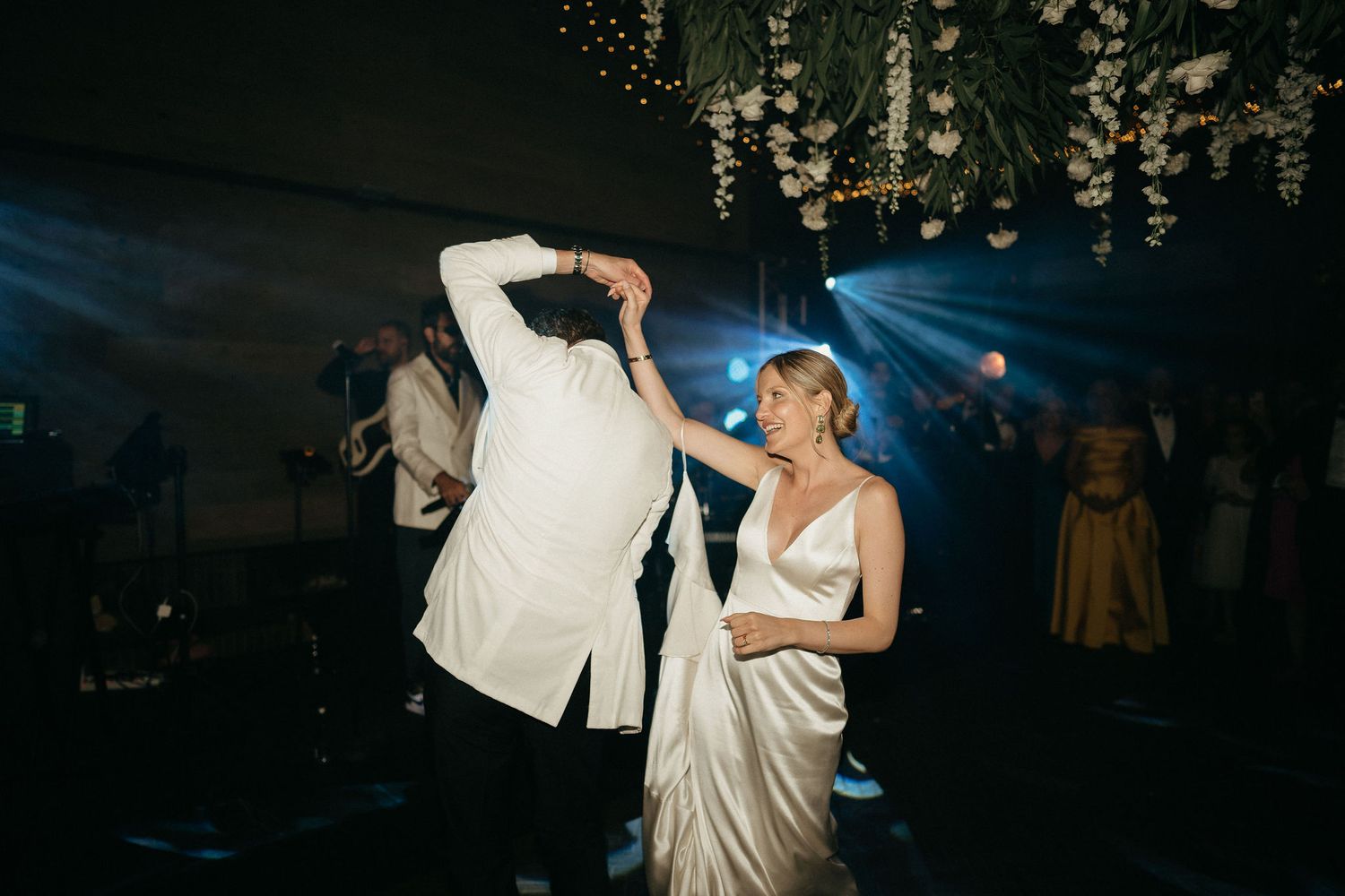 A couple dances together at an elegant wedding reception under crystal chandeliers.