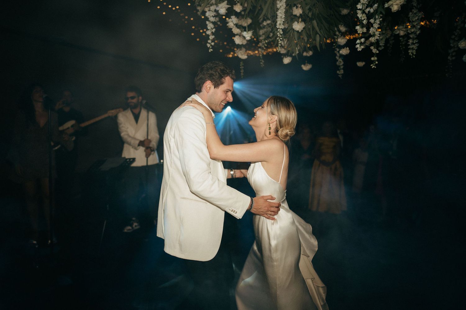 A couple shares a romantic dance at their wedding reception in a dimly lit venue with atmospheric lighting.