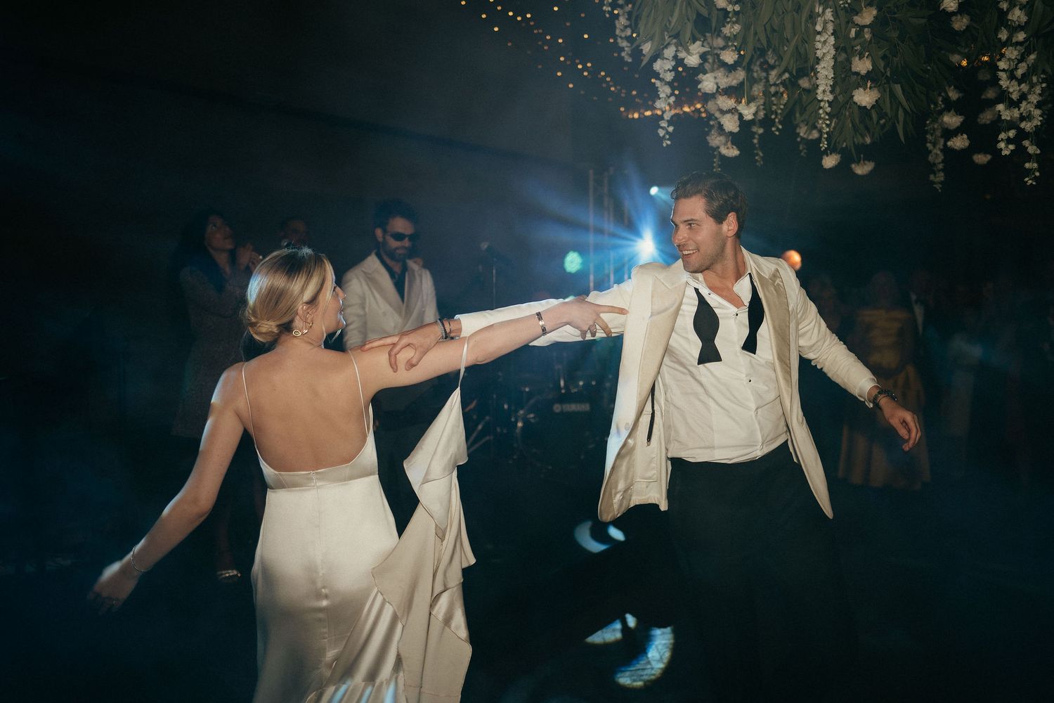 Wedding guests dance and celebrate on a dark dance floor illuminated by twinkling lights above.