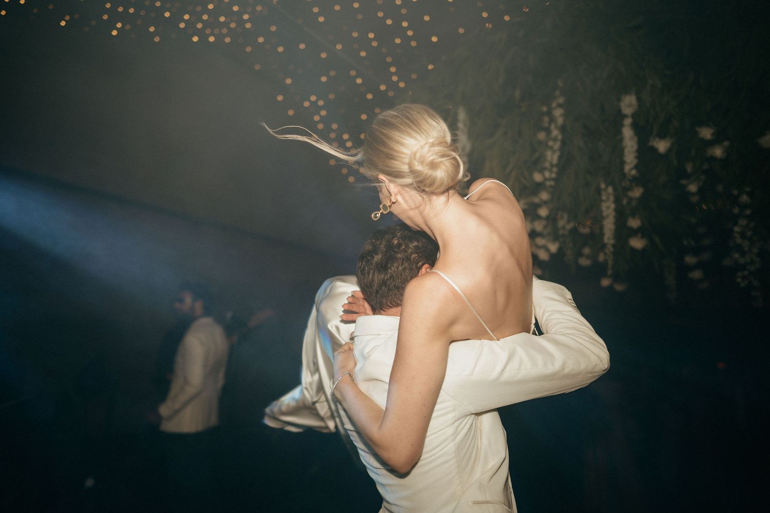 Couples dance and embrace during a romantic wedding reception under twinkling lights and floral decorations.