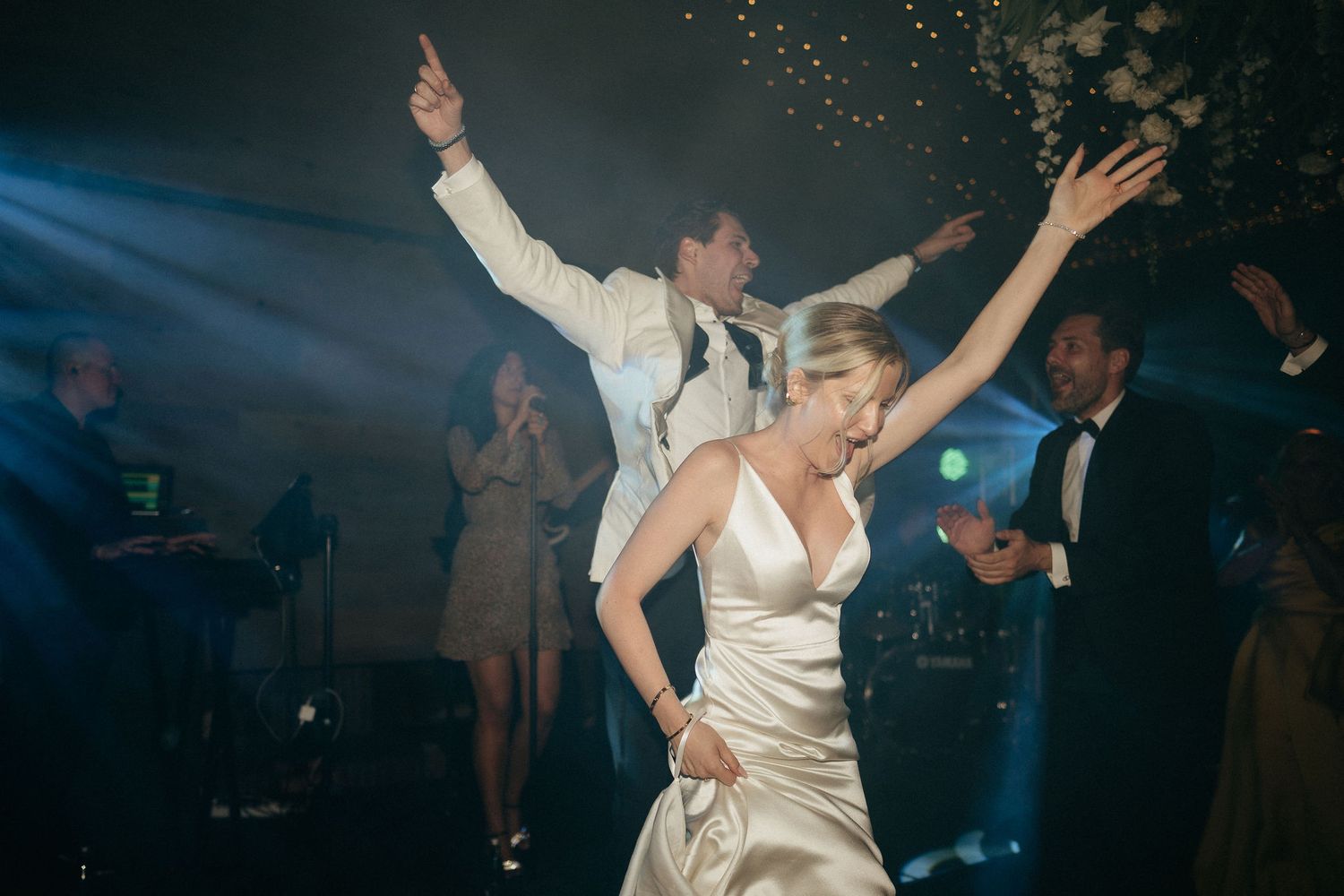 A couple dances together during their wedding reception as guests look on in a dimly lit ballroom.
