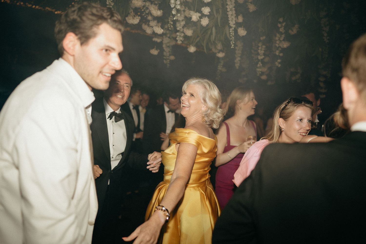 A group dances and celebrates at a formal event in a dimly lit venue.