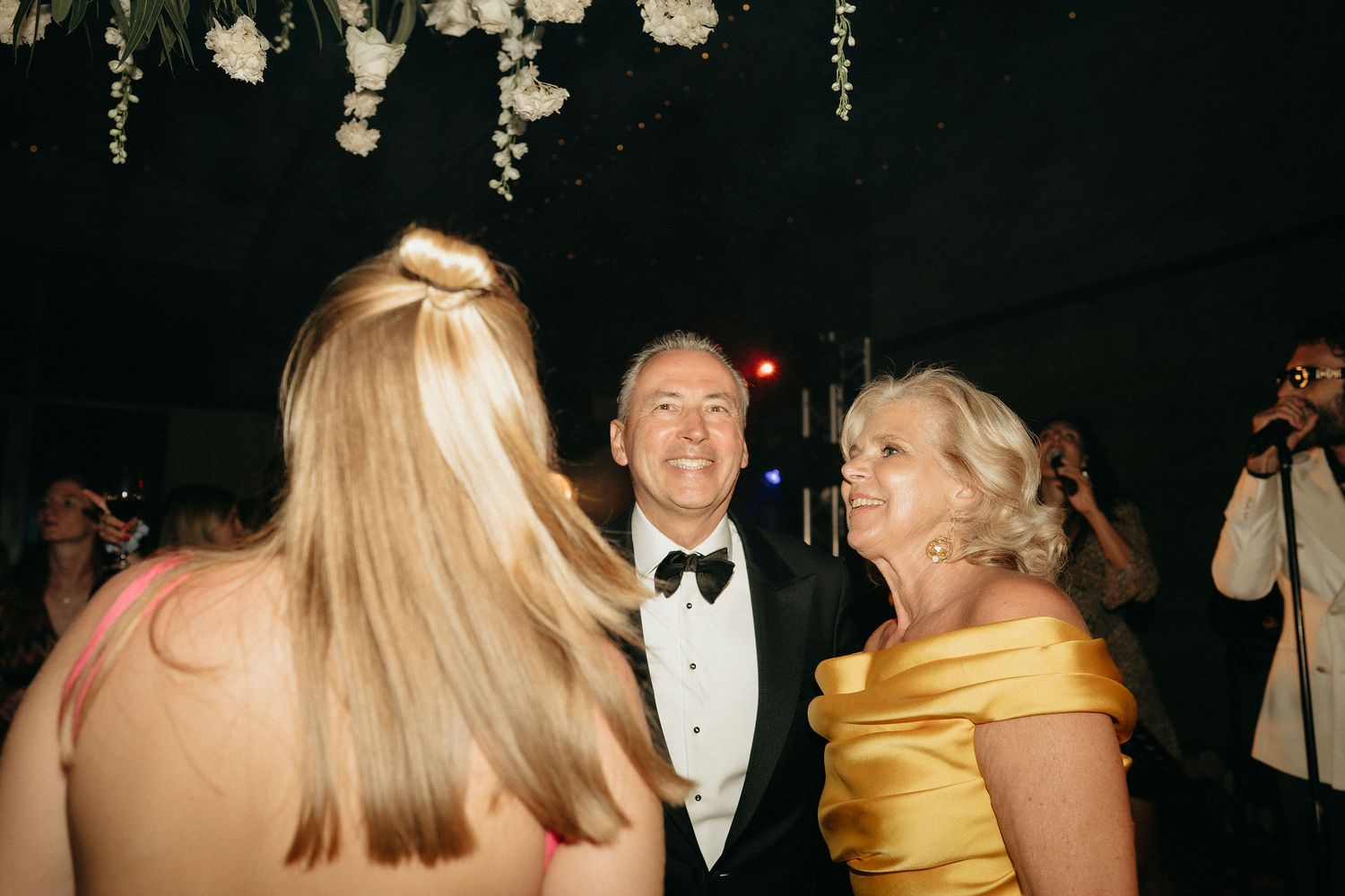 People dancing and celebrating at a formal event in a dimly lit venue with elegant attire.