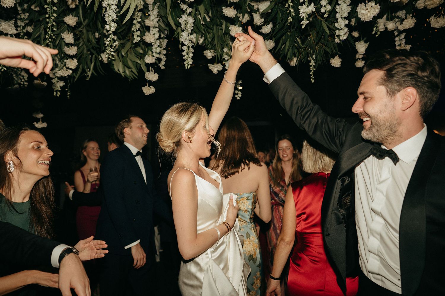 People dancing and celebrating at a lively wedding reception party under dim lighting.
