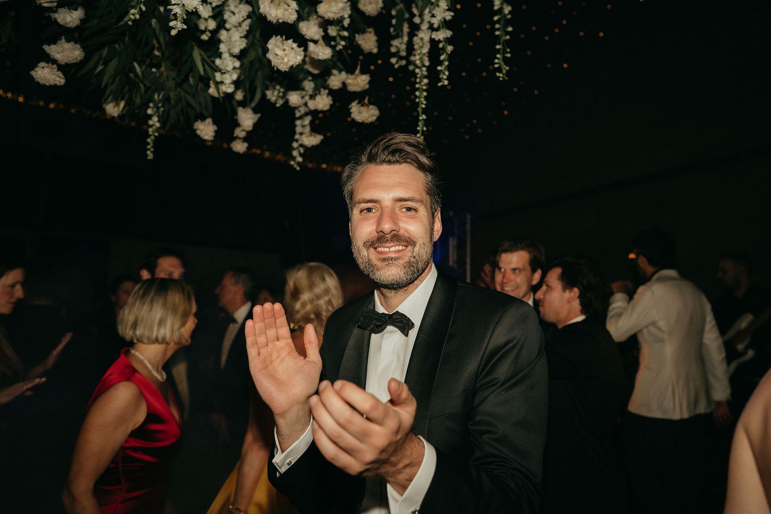 A group of people dancing and celebrating at a dimly lit party or wedding reception.