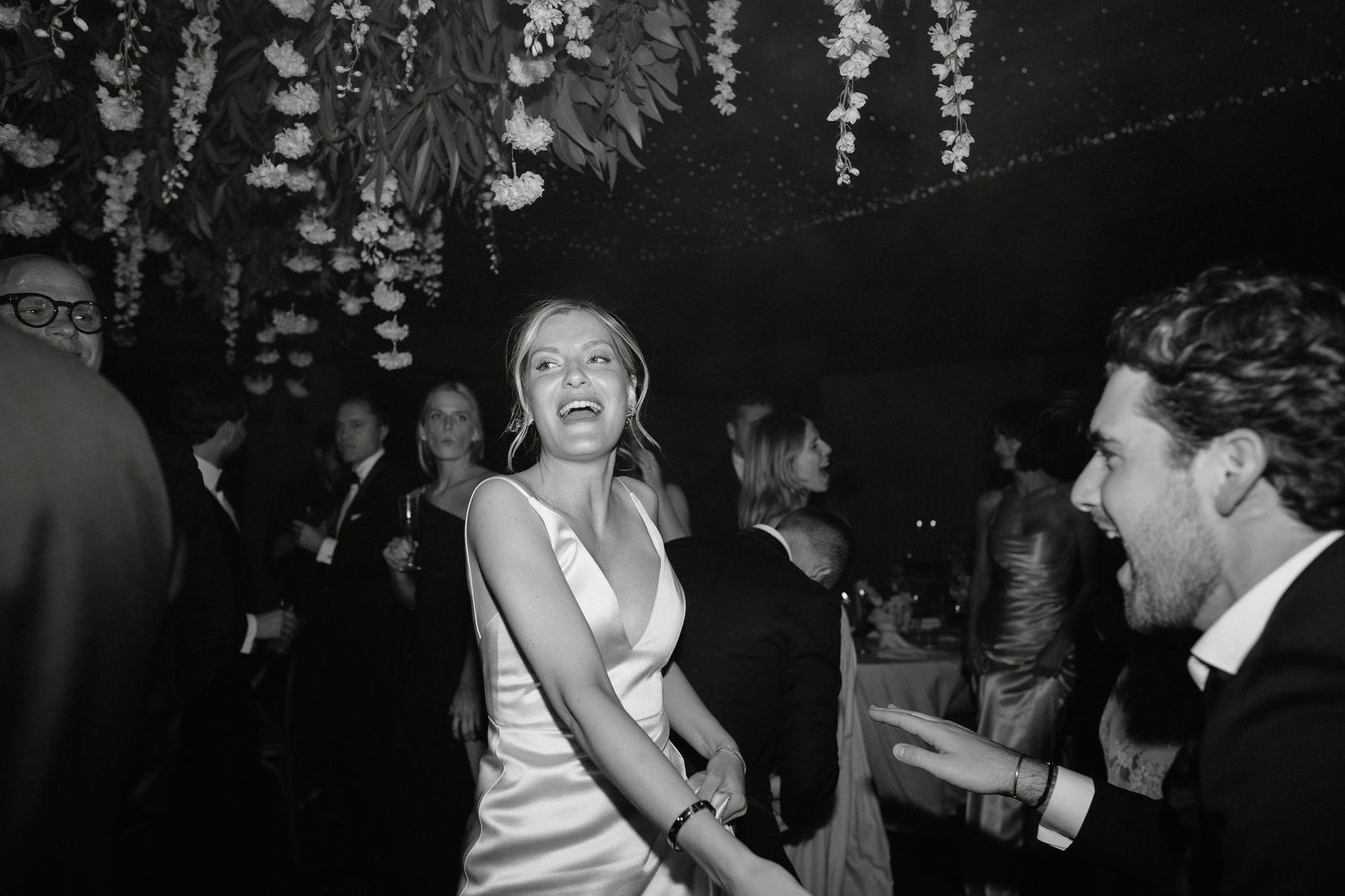 A candid black and white party scene shows people dancing and laughing at an elegant evening celebration.