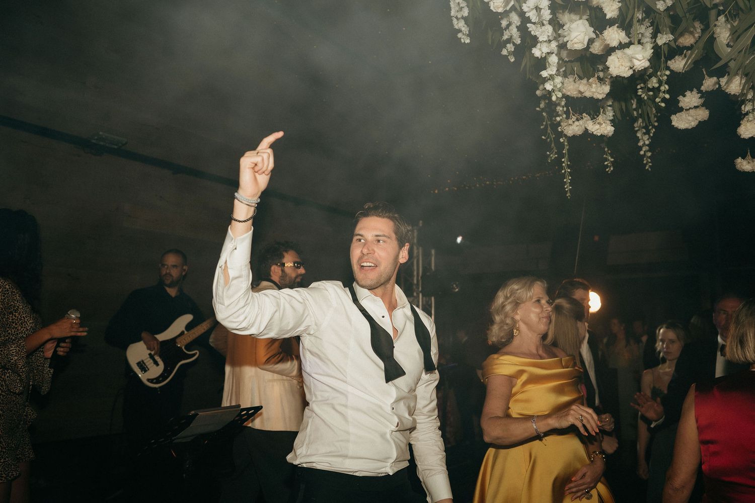 Wedding guests dancing and celebrating on a dark dance floor with dramatic lighting.