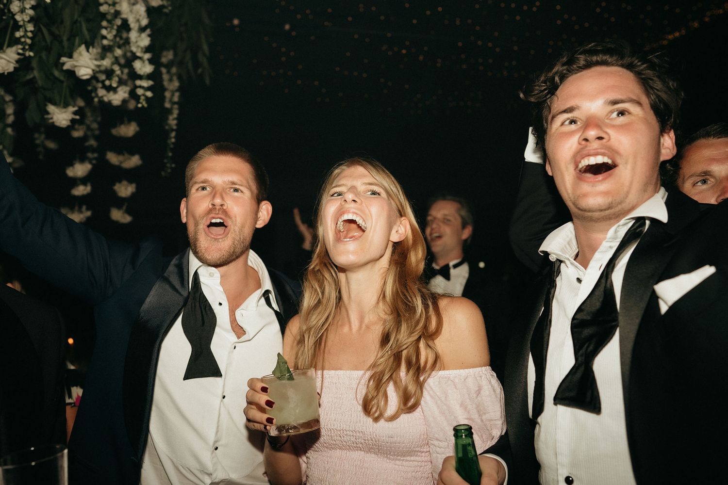 Party guests laugh and celebrate together while holding drinks at a nighttime event.