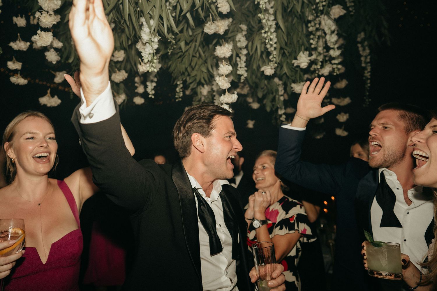 Guests dance and celebrate at an elegant formal event with people dressed in black tie attire.