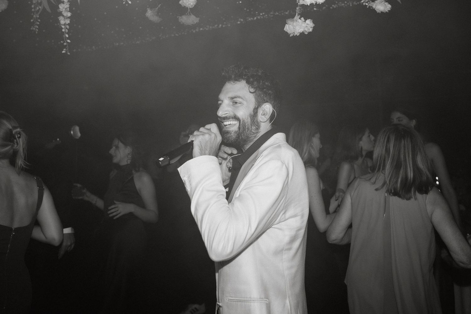 People dance and celebrate at a dark nightclub or party venue with atmospheric lighting.