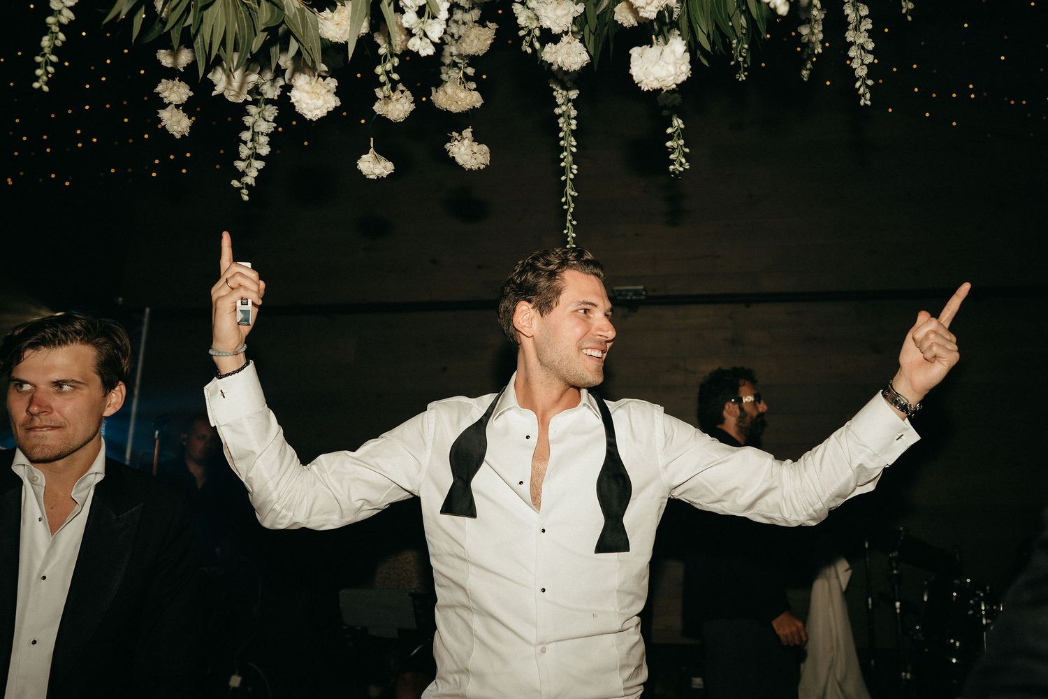 A performer in a white shirt dances energetically on stage with raised arms during a live performance.