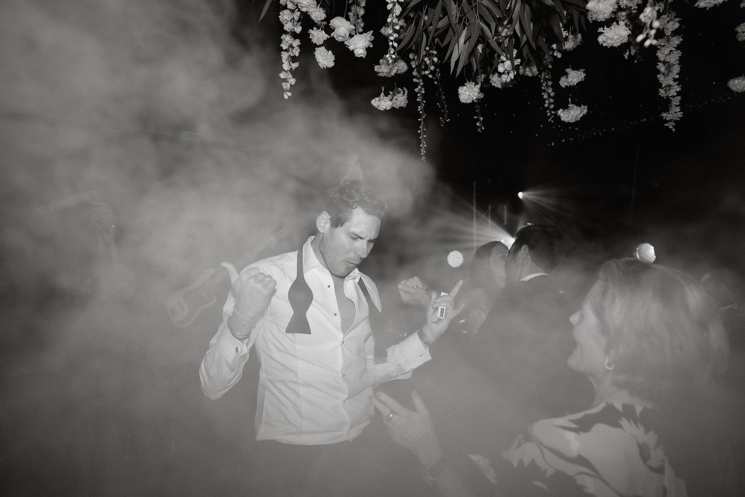 A group of people sit together in a dimly lit room with atmospheric fog or smoke creating a moody ambiance.