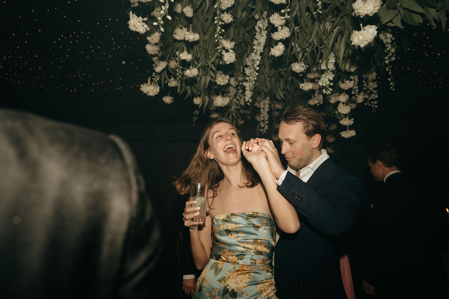 A couple shares a joyful moment together at a dimly lit wedding reception with hanging lights overhead.