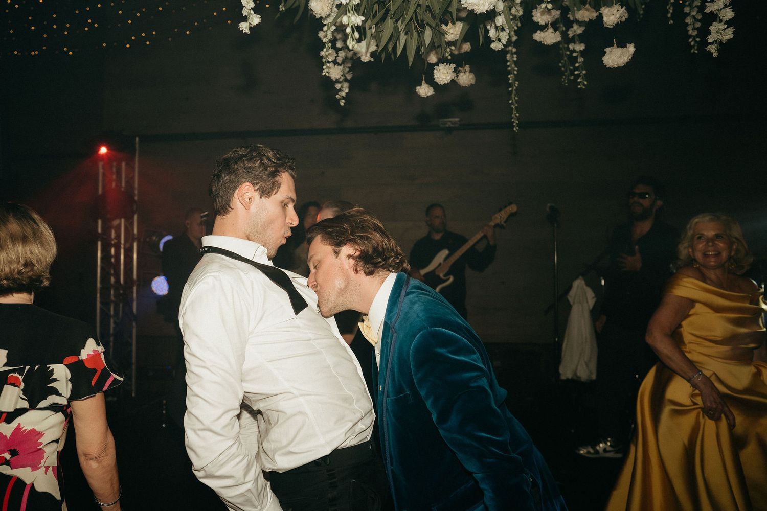 Wedding guests dance and celebrate together on a dark dance floor during an evening reception celebration.
