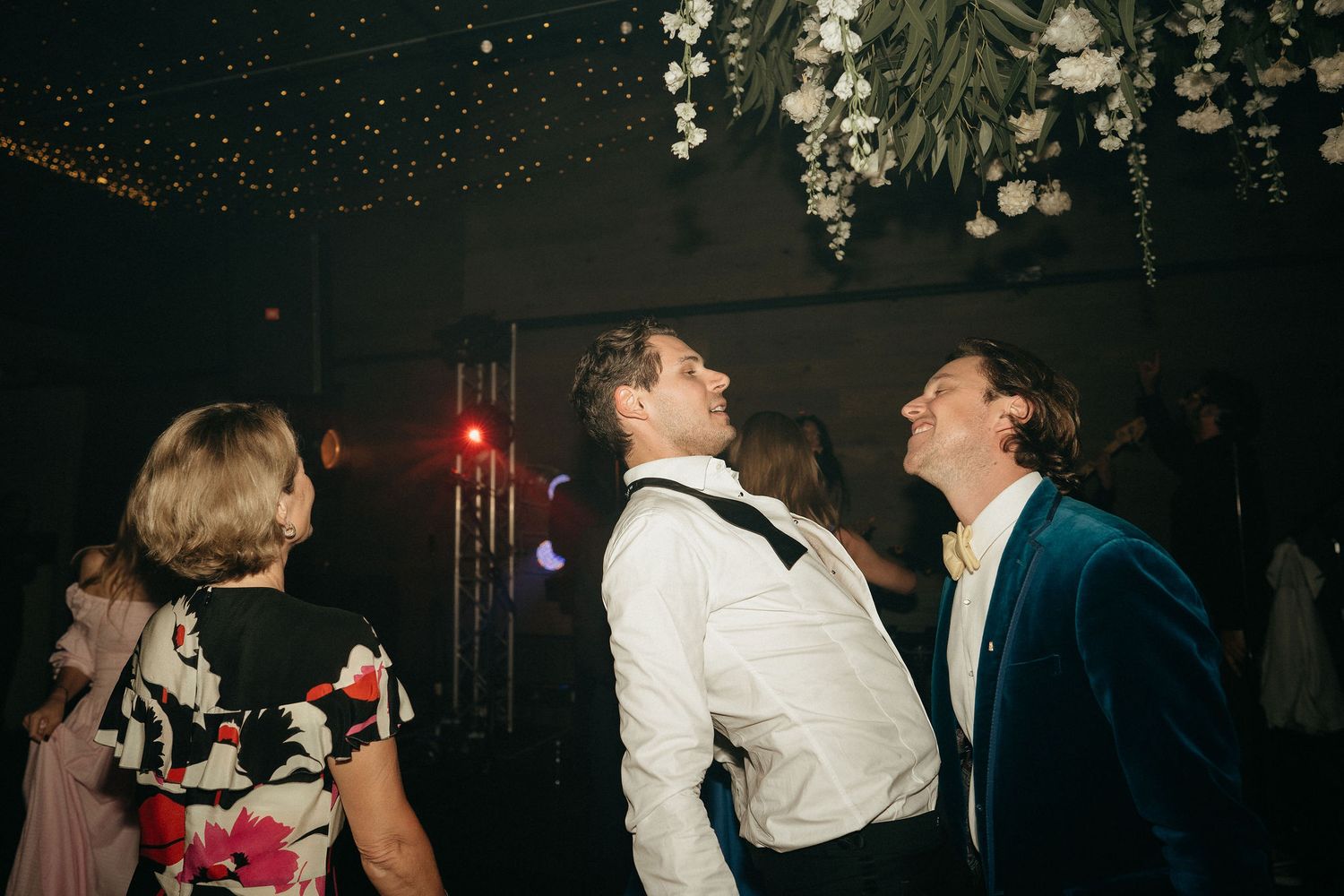 People dancing and laughing together at a wedding reception under dim lighting and decorative ceiling details.