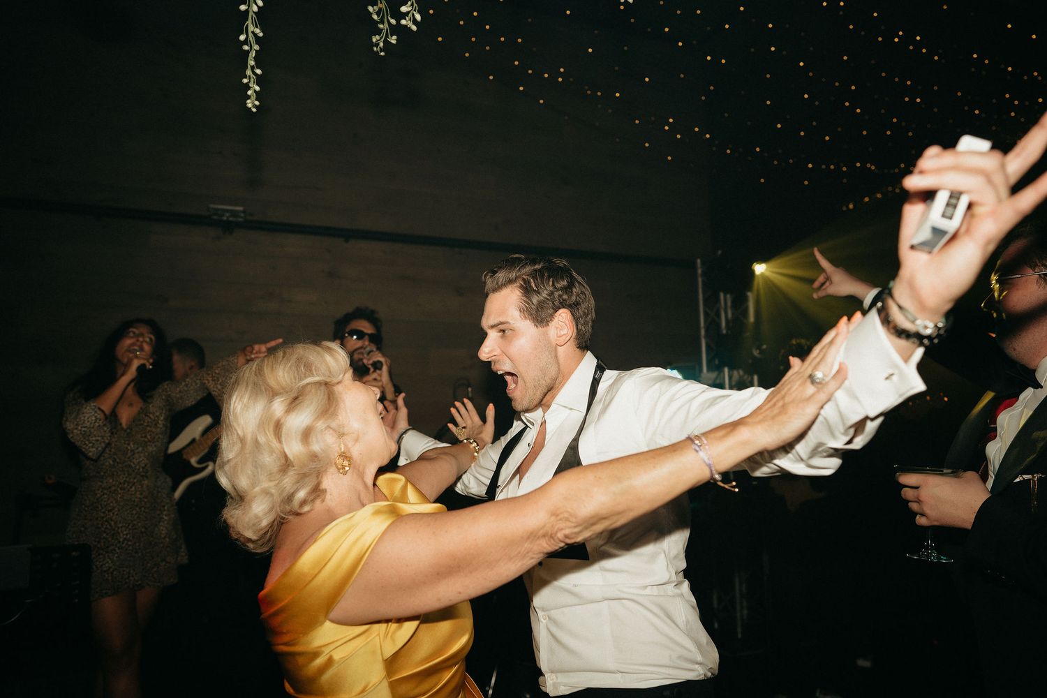 People dancing together in a dark nightclub or party venue with energetic movements and raised arms.