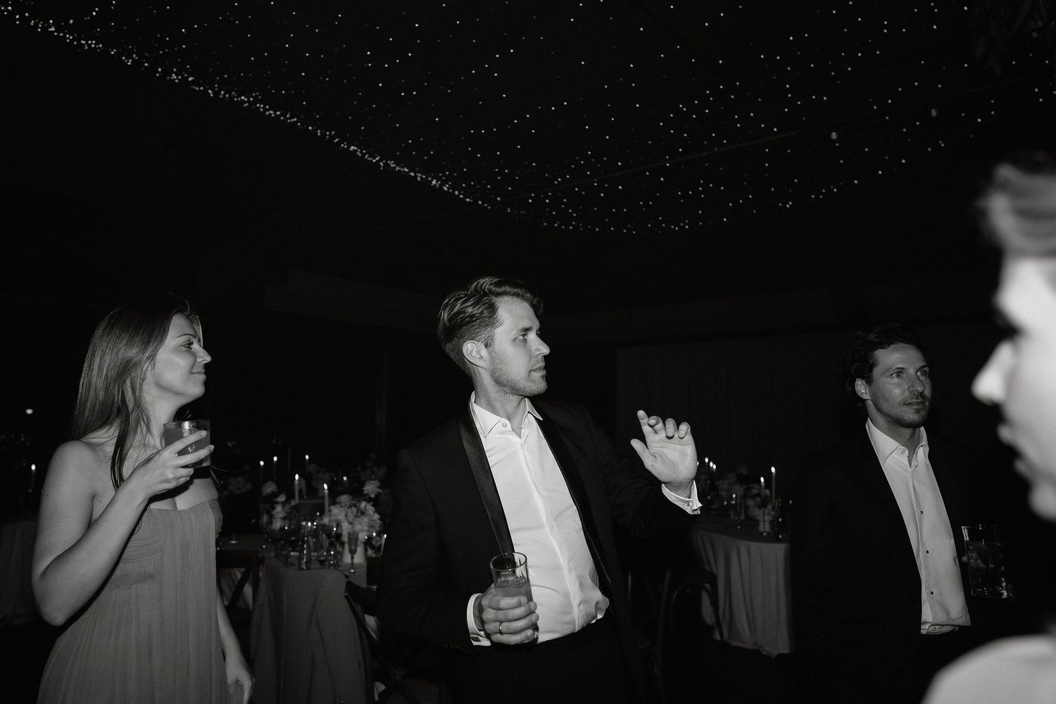 Black and white photo of people dancing and socializing at a formal evening event with drinks in hand.