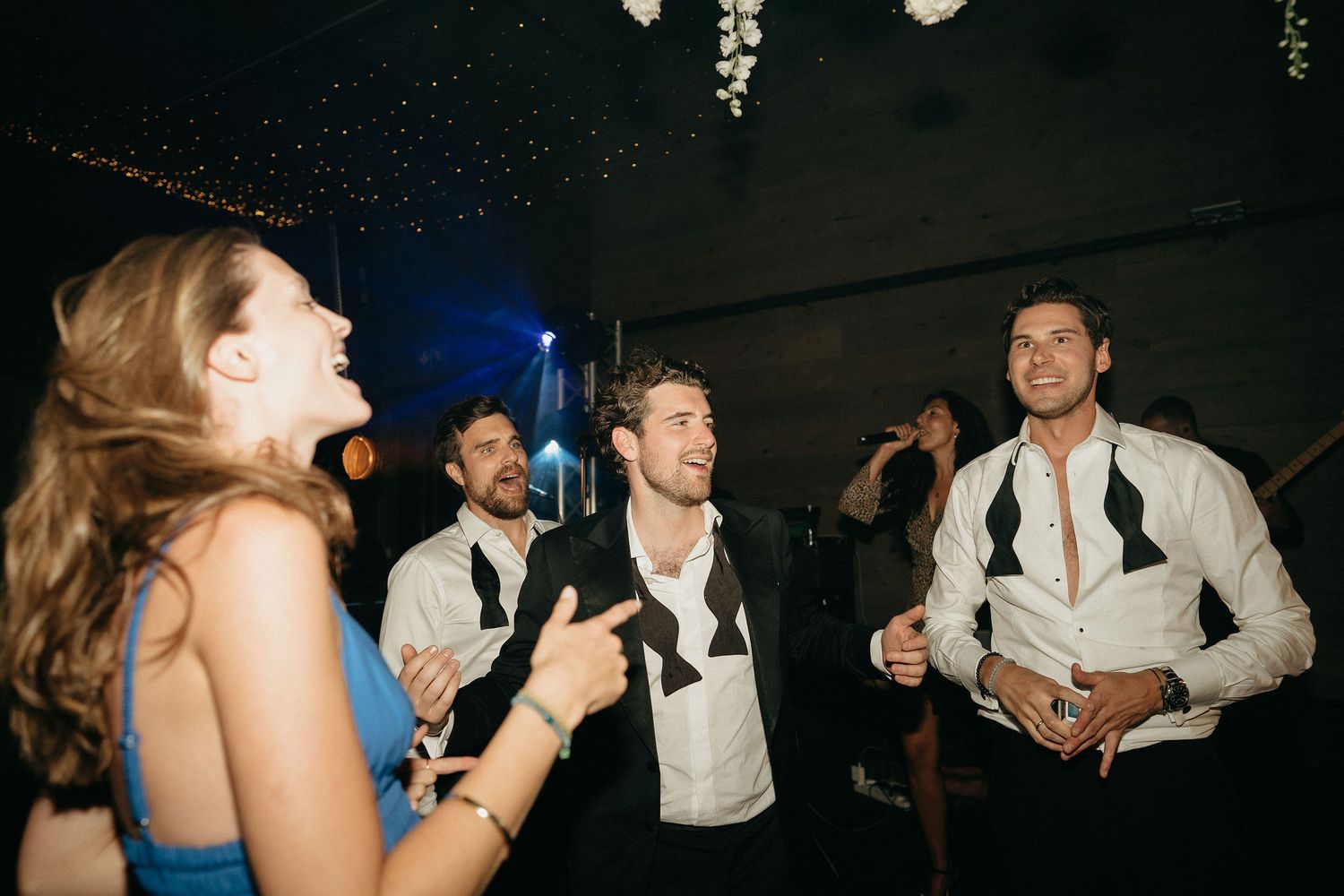 Wedding guests dance and celebrate on a dimly lit dance floor during an evening reception.