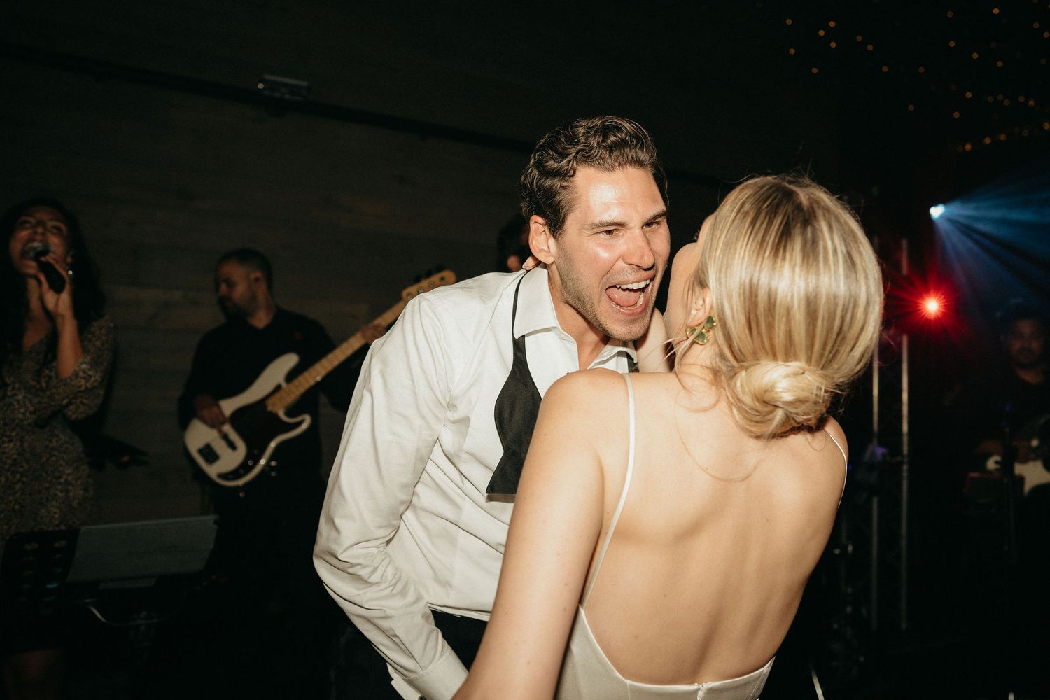 A couple shares an intimate dance moment at a dimly lit reception with live music in the background.