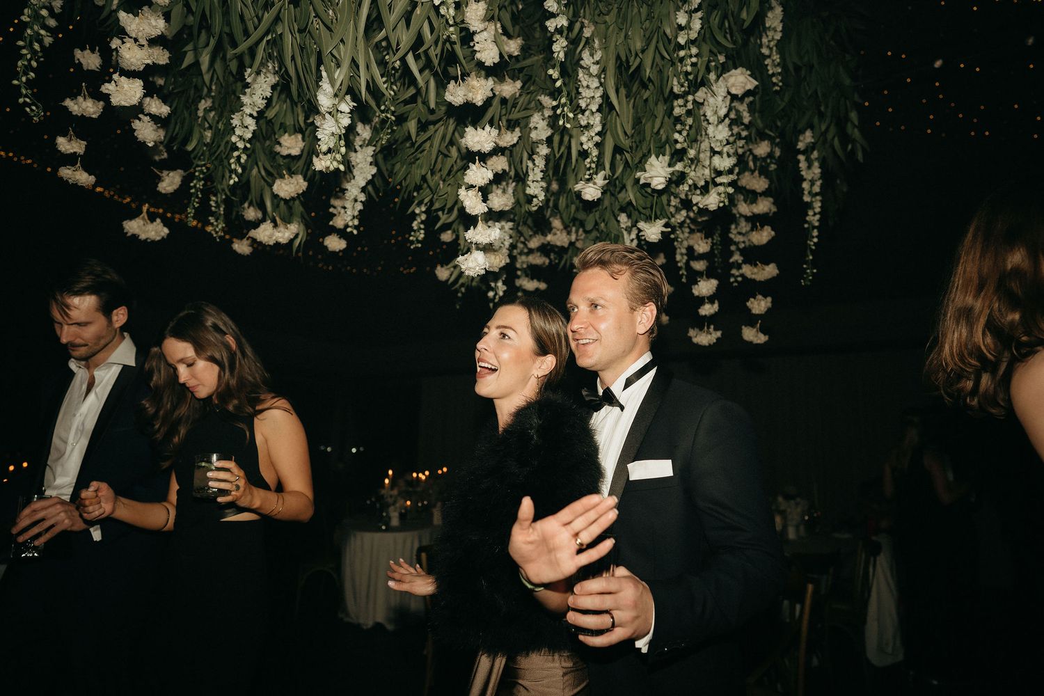 Guests mingle and dance at an elegant evening reception with glowing lights in the background.
