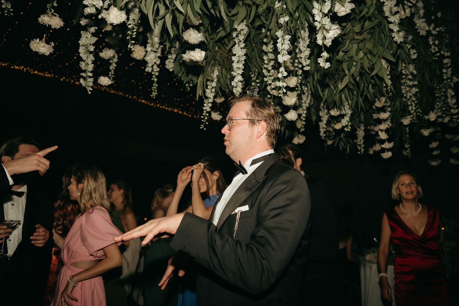 People dancing together at a dimly lit party or celebration with decorative lights hanging from above.