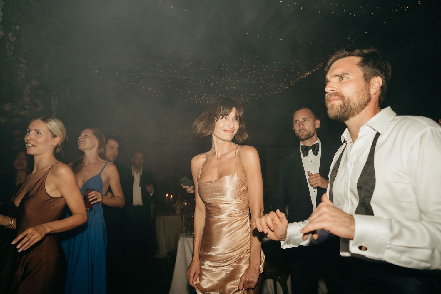 Wedding guests dance and celebrate together on a dimly lit dance floor during an evening reception.