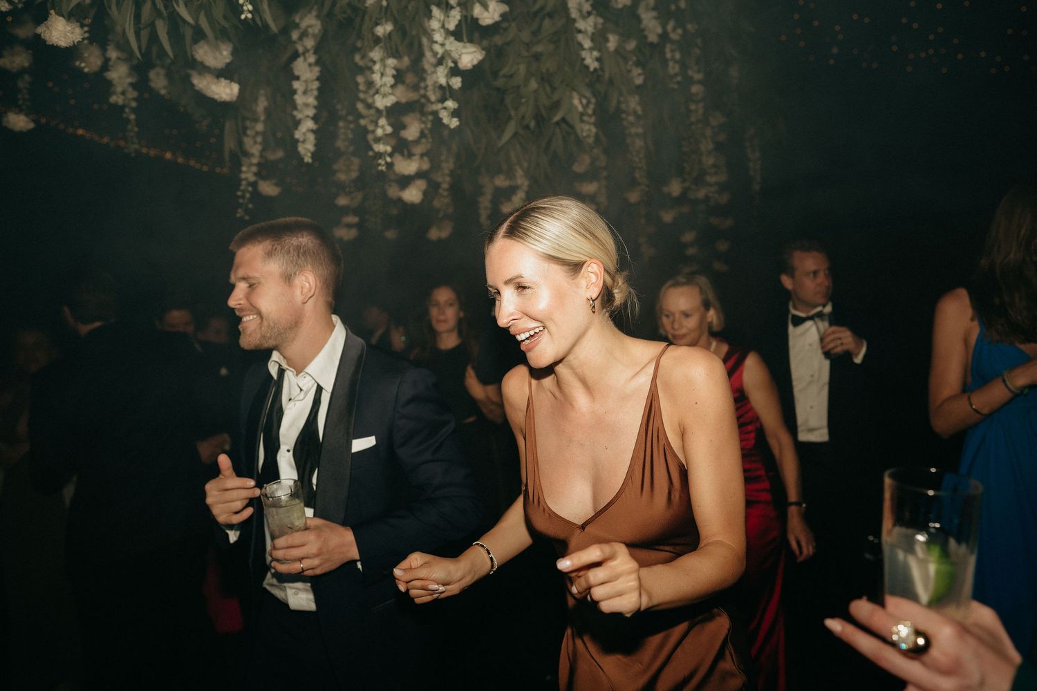 People dancing and socializing at a dark nightclub or party venue with atmospheric lighting.
