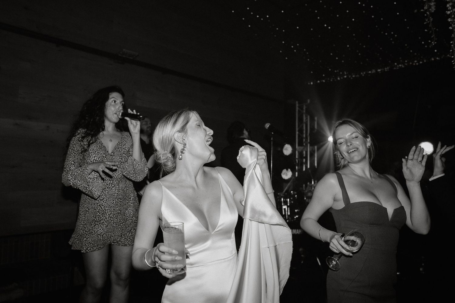 People dancing and socializing at a dark indoor wedding reception venue.