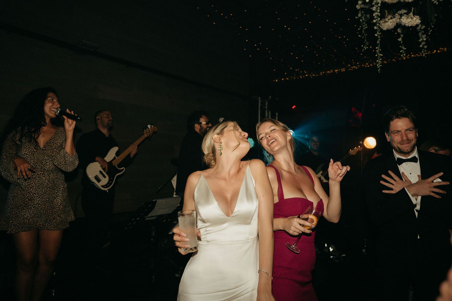 Wedding guests dancing and celebrating on a dimly lit dance floor at an evening reception.