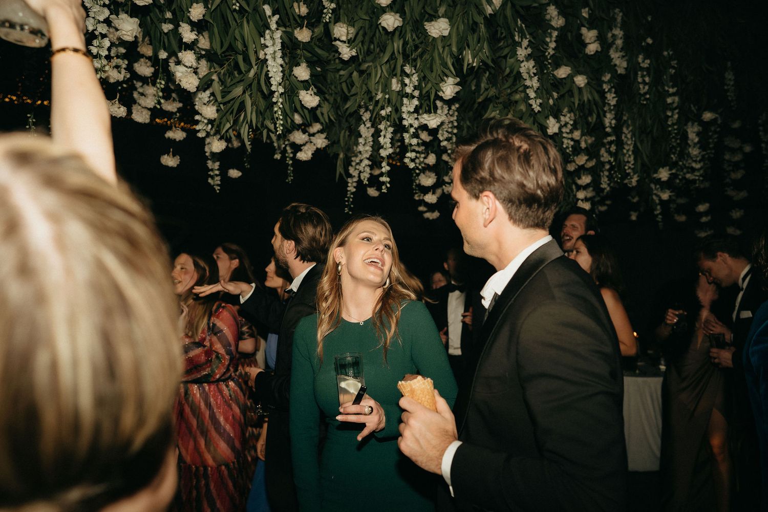 Wedding celebration under hanging floral decorations in a dark reception venue.