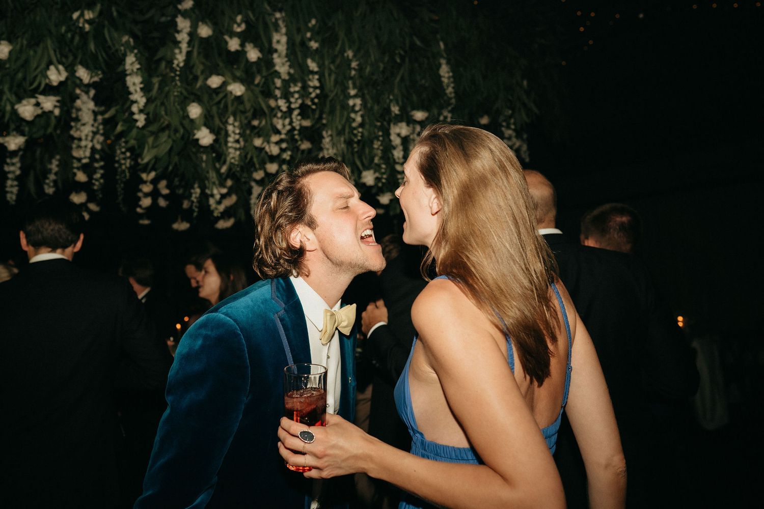 Guests enjoying themselves on a dance floor with decorative lighting and greenery overhead.