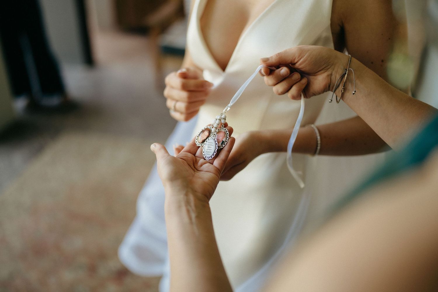 Close-up view of hands adjusting jewelry and dress details during wedding preparations.
