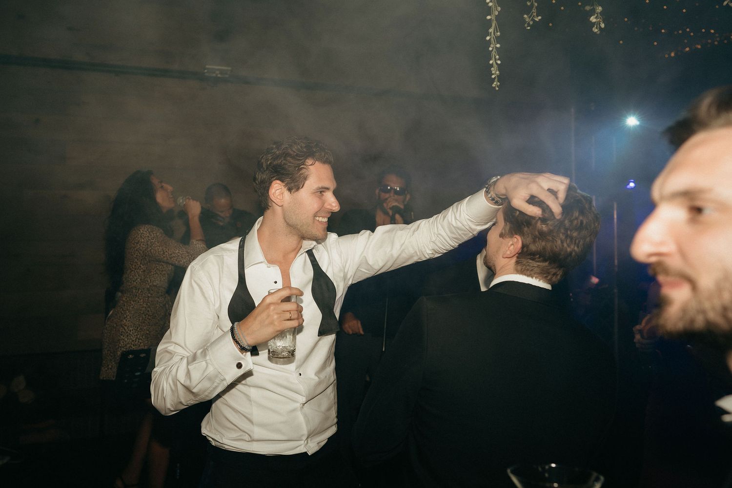 A group of people dancing and celebrating at a dimly lit party venue with atmospheric lighting.