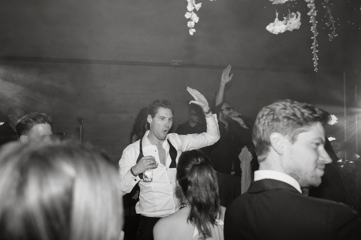 Wedding guests dance and celebrate together on a dark dance floor with decorative lighting.