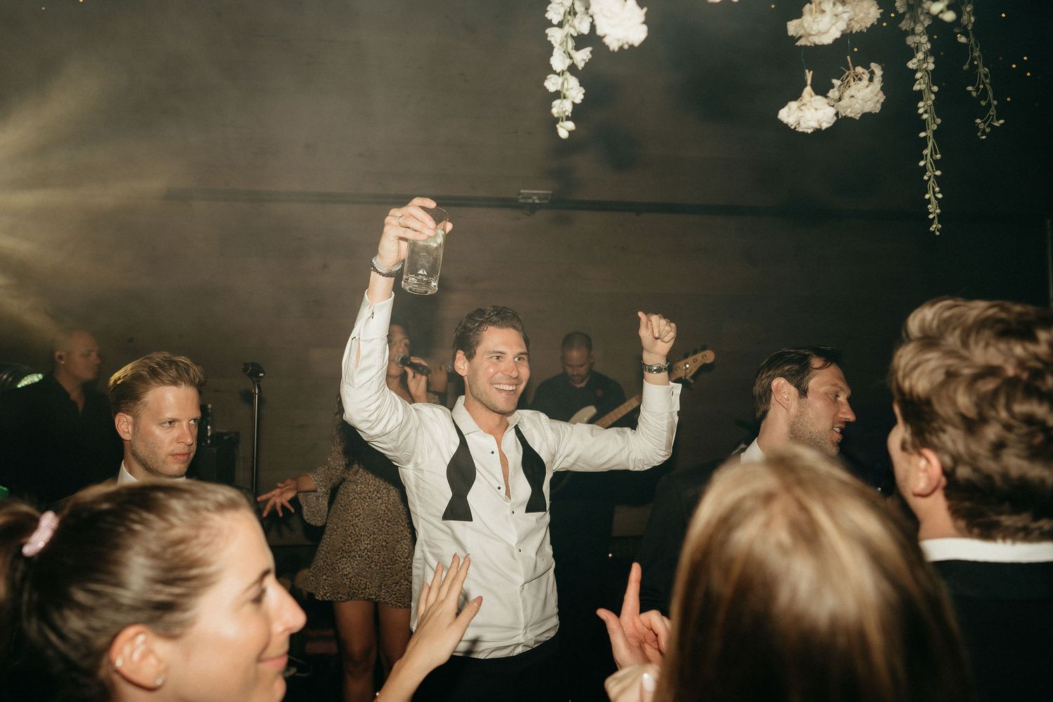 Wedding reception dance floor filled with guests enjoying themselves under dim lighting and floral decor.